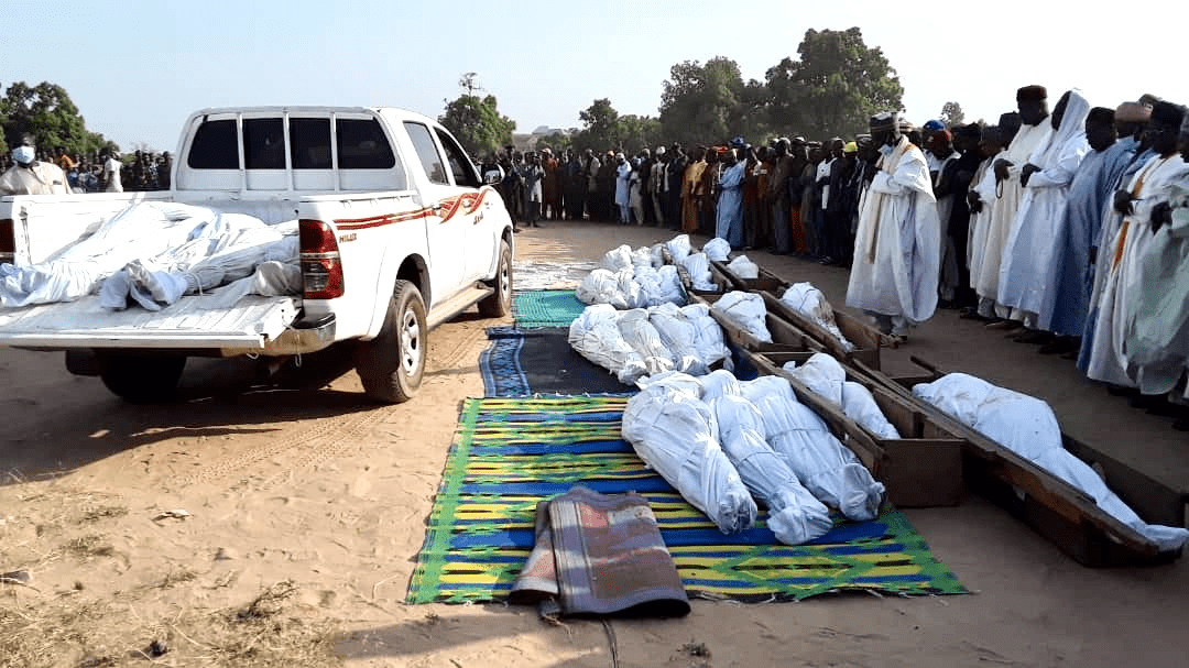 A group of people in traditional attire attending an outdoor ceremony with covered bodies laid out on the ground.