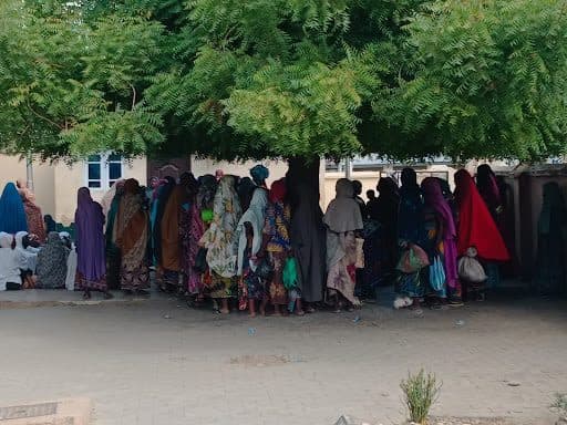 Group of people in colorful clothing huddled under a shady tree.