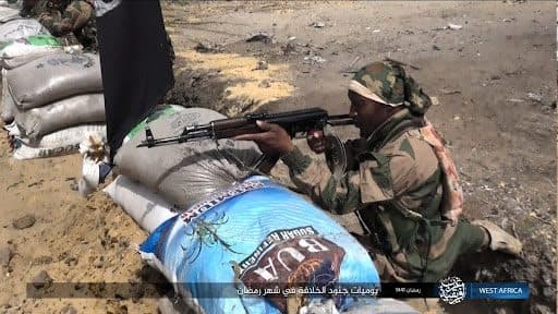 A soldier in camouflage aiming a rifle behind sandbag barricades.
