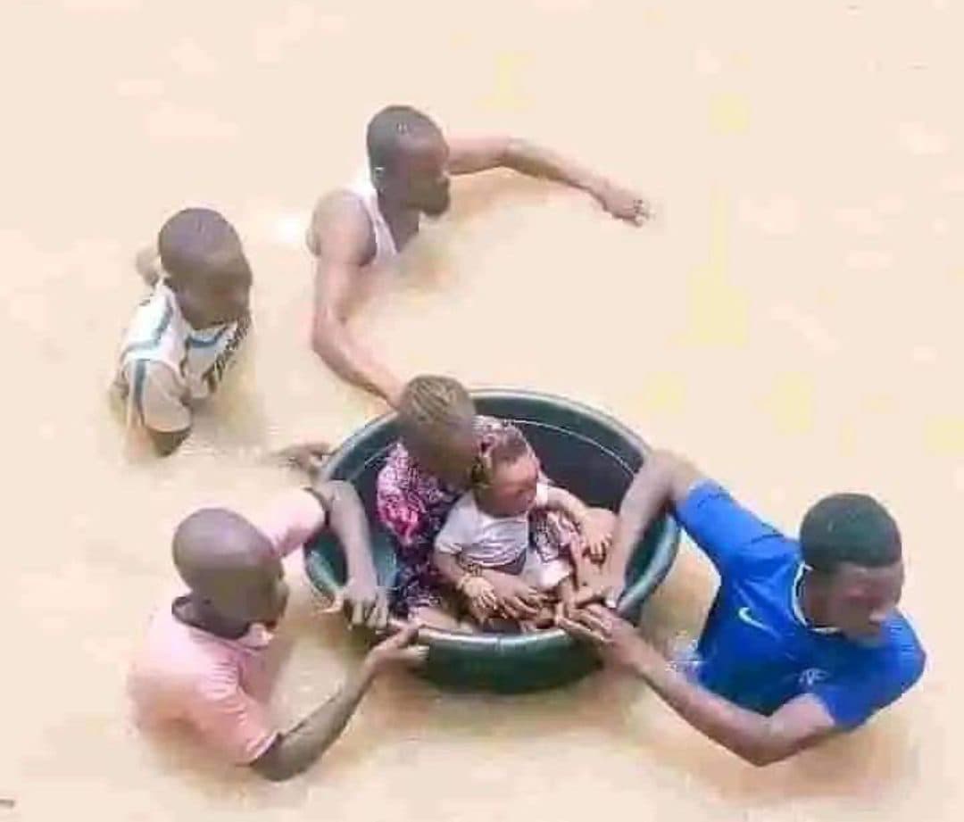 People using a large basin to float through a flood, aiding others in the water.