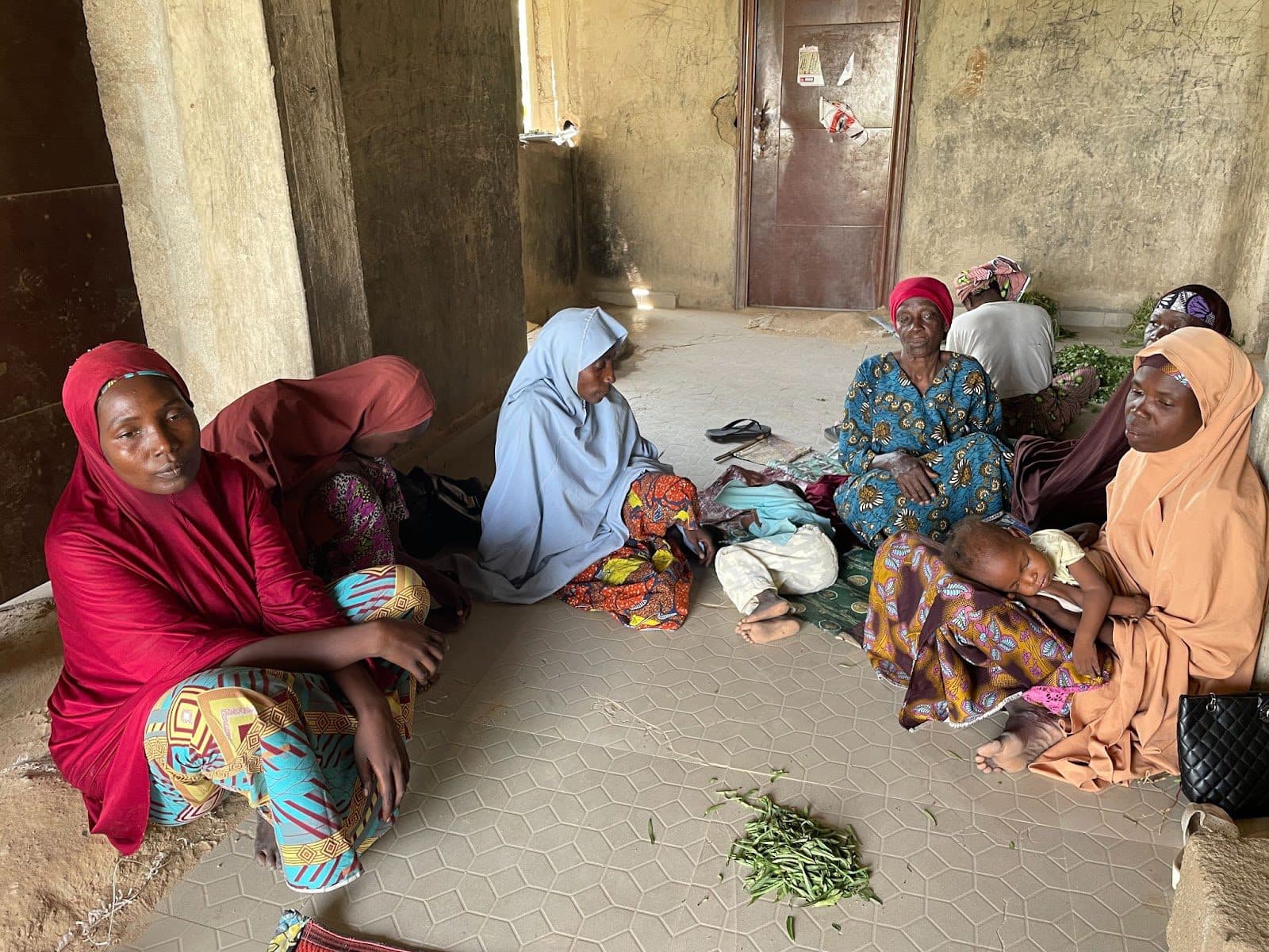 Group of women sitting on the floor in traditional attire with a child sleeping on one of the women's lap.