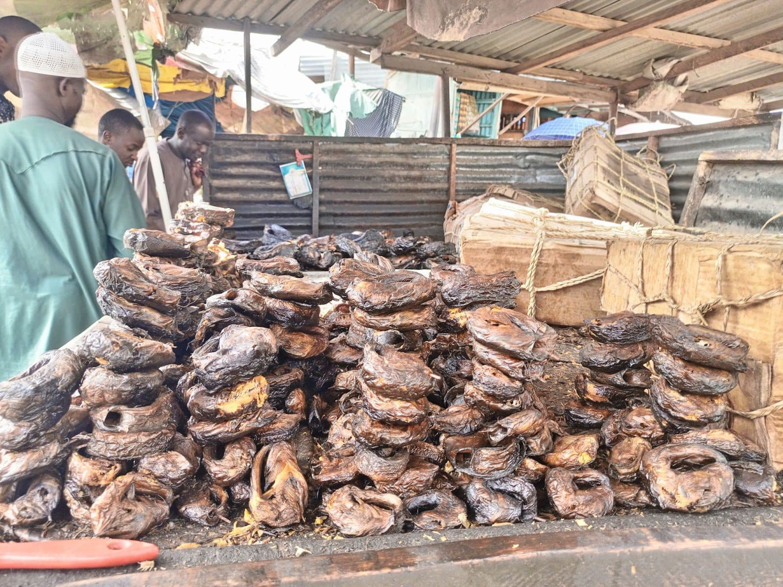 A pile of dried fish for sale at a market stall with customers in the background.