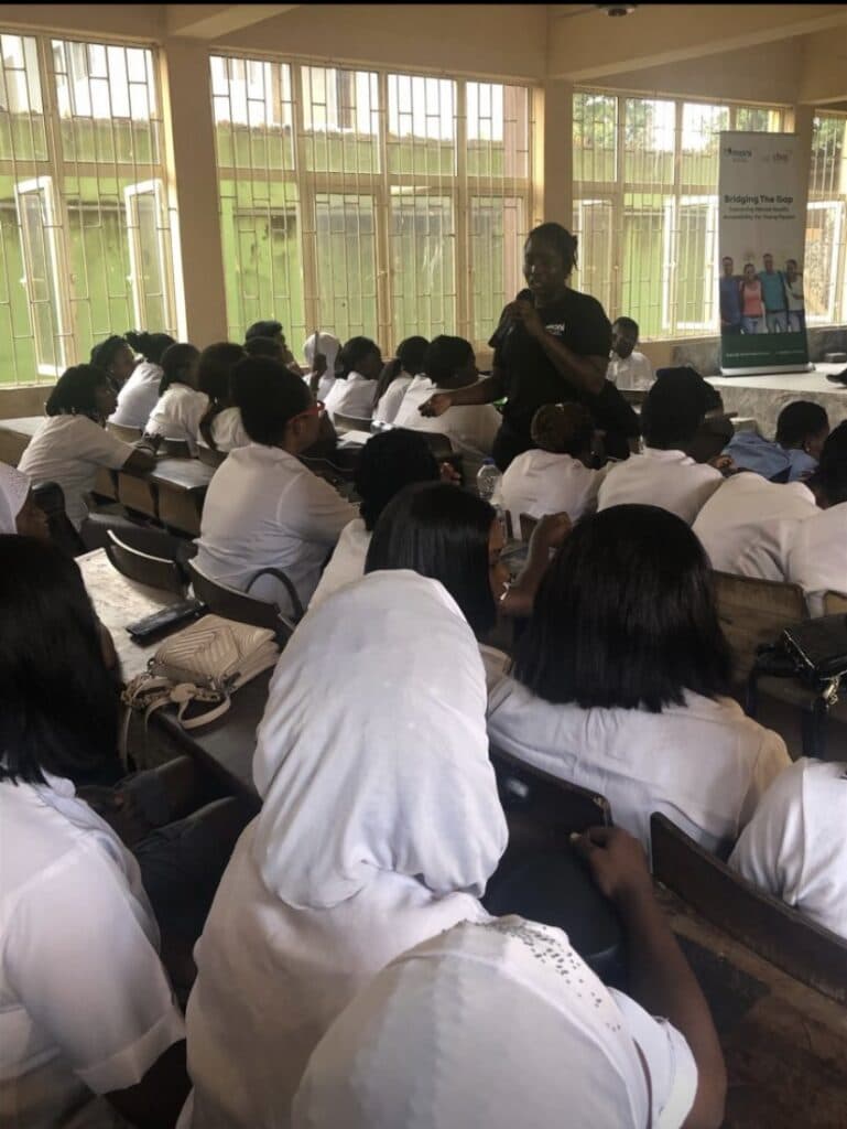 A speaker addressing a room full of seated students in white uniforms.