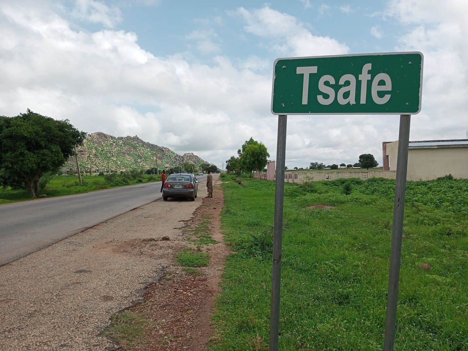 Green road sign reading "Tsafe" by a roadside with cars and lush greenery.