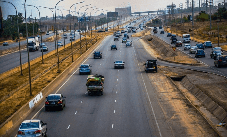 Vehicles travel on a multi-lane highway with streetlights and a clear sky.