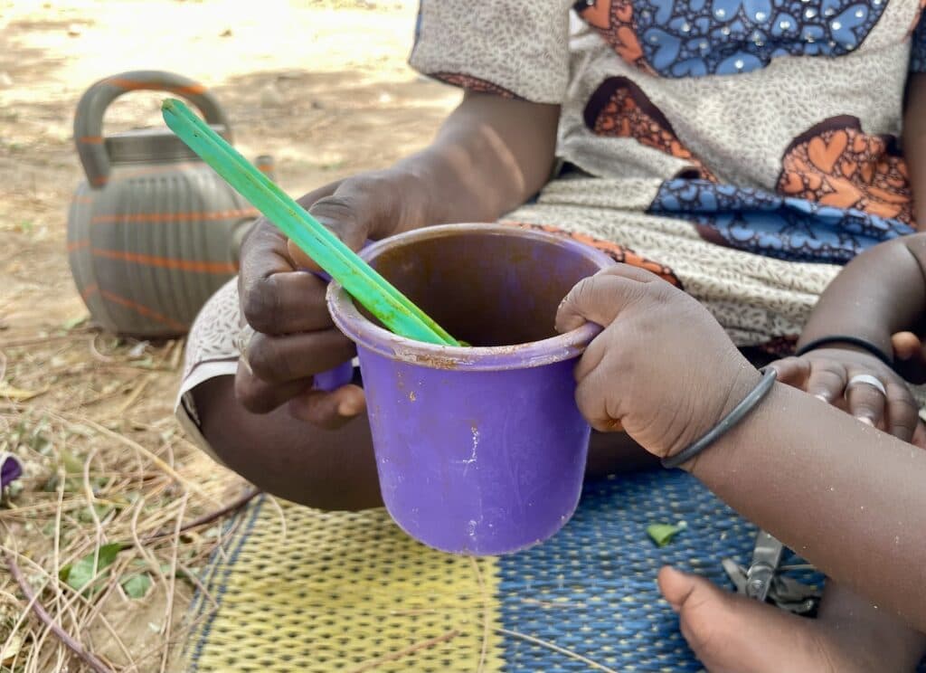 Woman and child holding a purple cup with a green spoon, with a kettle in the background.