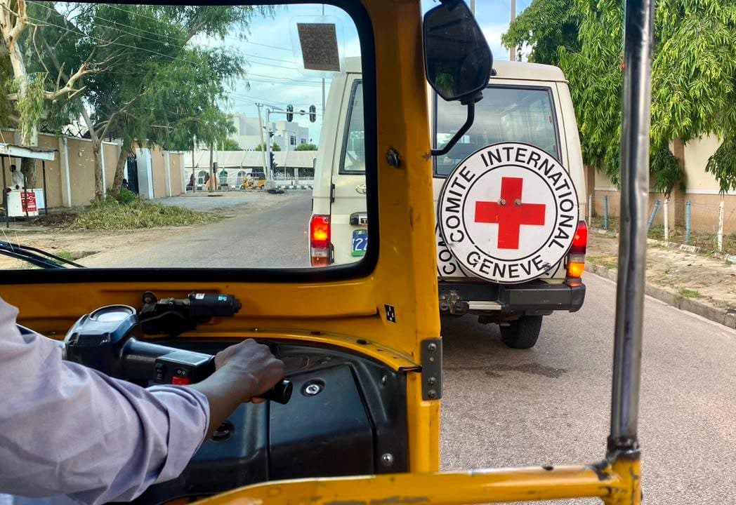 View from inside an auto rickshaw looking at a Red Cross vehicle on the road.