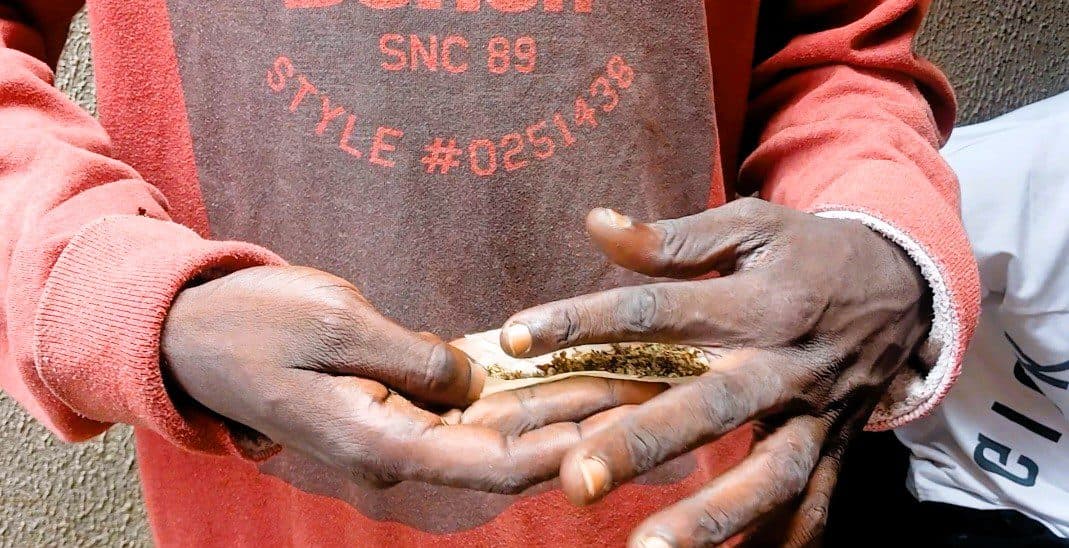Person in a red sweater rolling a cigarette with tobacco in their hands.
