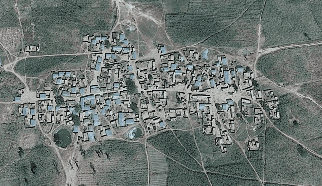 Aerial view of a clustered village with irregular building patterns surrounded by fields.