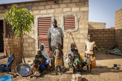 A family in front of a brick house with a man standing, woman seated and children around them in a rural setting.