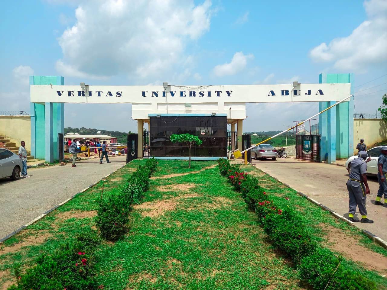 Entrance gate of Veritas University Abuja with people and cars nearby.