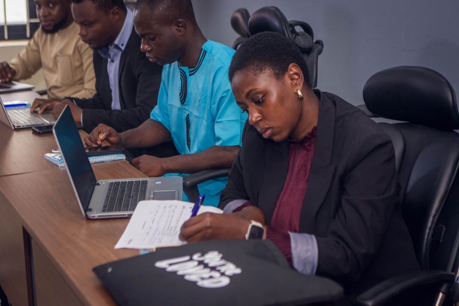 Professionals focused on laptops and notes during a business meeting or training session.
