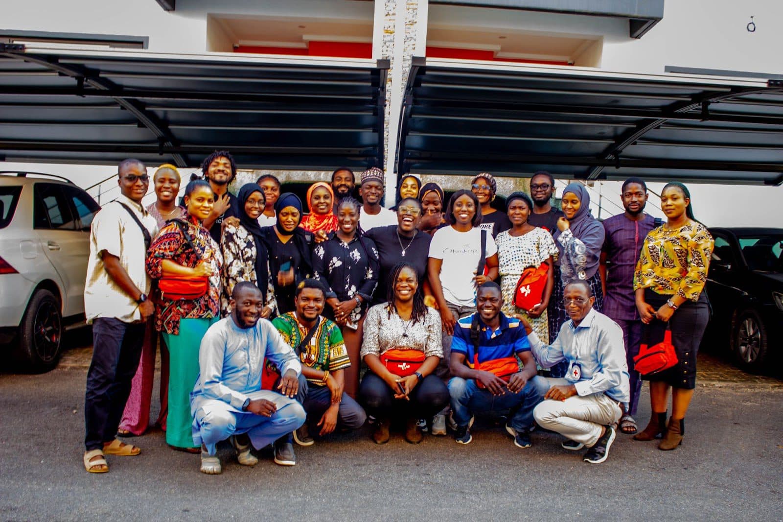 Group of smiling people posing together outdoors, some in traditional attire.