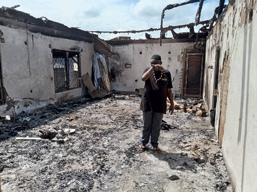 Man standing amidst the ruins of a burnt building, covering his nose.