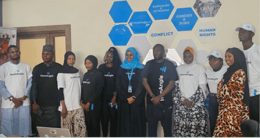 Group of individuals in branded t-shirts standing in front of a wall with hexagonal designs about social issues.