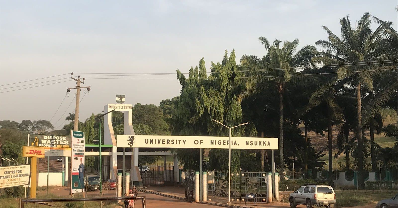 Entrance of University of Nigeria, Nsukka, with palm trees and signage.