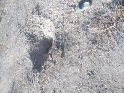 A hole in dry, uneven ground with sparse grass. Partial view of a shoe in the top right corner.