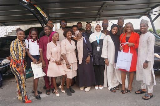 Group of people smiling and posing under a carport, some holding bags.
