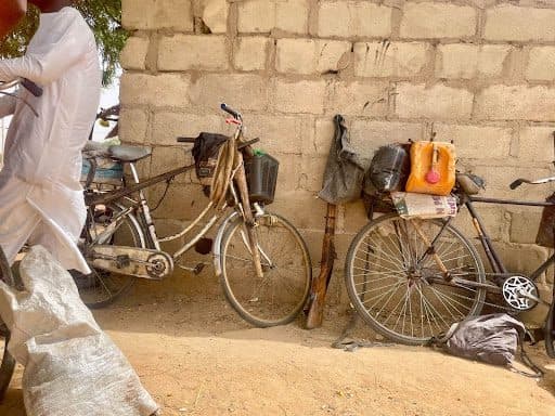 Two bicycles loaded with bags and containers lean against a stone wall. A person in white clothing is partially visible.