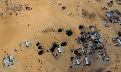 Aerial view of a desert village with scattered buildings and sparse vegetation.