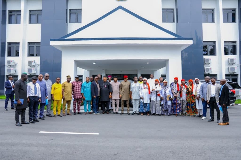 A group of people stands in front of a modern building, posing for a photograph on a paved road.