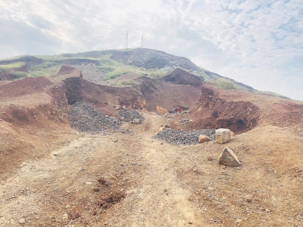 Rocky landscape with eroded hills and sparse vegetation under a cloudy sky. Two small towers stand on the hilltop.
