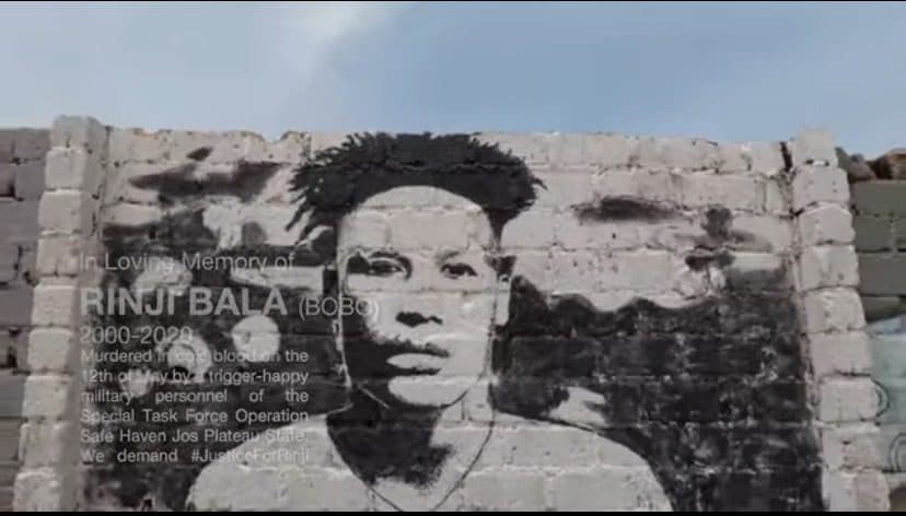 Mural on a brick wall depicting a person's face with a memorial text remembering Rinji Bala and calling for justice.