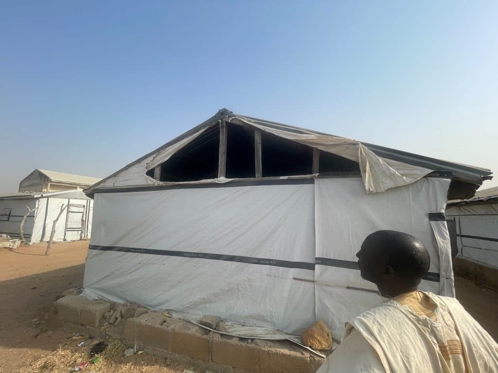 A person looks at a large, weathered tent structure under a clear blue sky.
