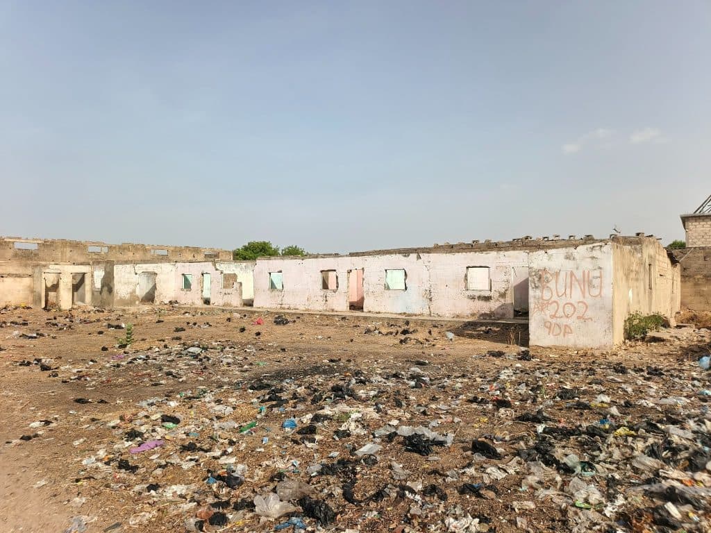 Abandoned building with graffiti in a littered, barren area under a clear sky.