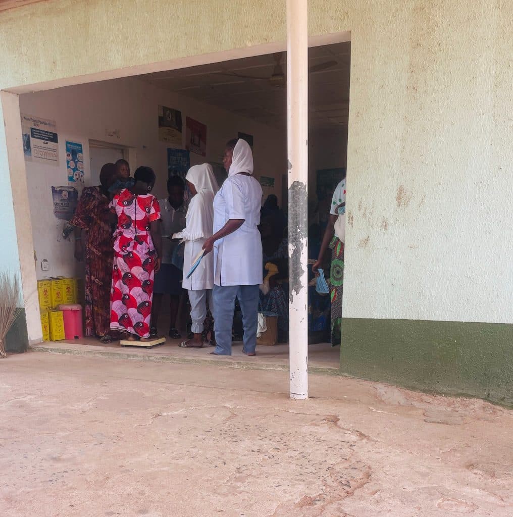 People gathered at a clinic entrance, with some in medical attire and others waiting in colorful clothing.