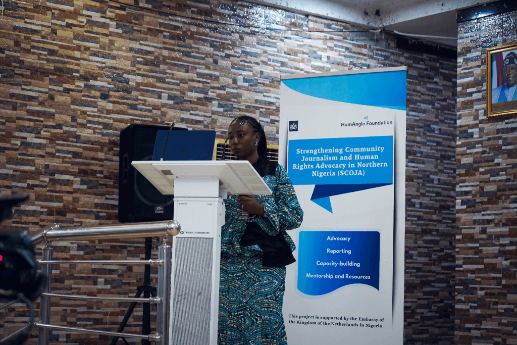 A woman speaks at a podium next to a banner about strengthening journalism and human rights advocacy in Northern Nigeria.
