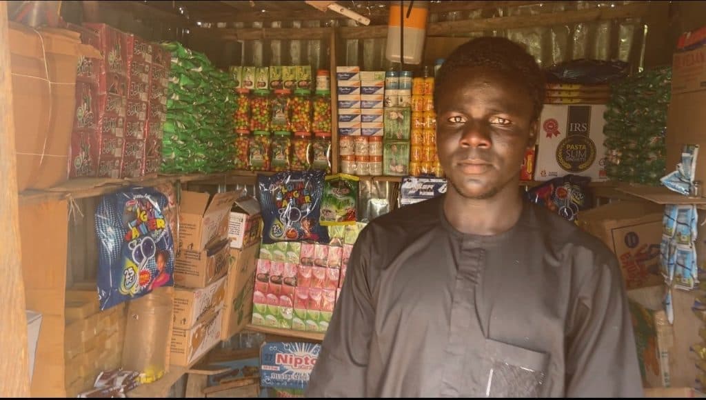 Person standing in front of shelves stocked with various packaged goods in a small shop.