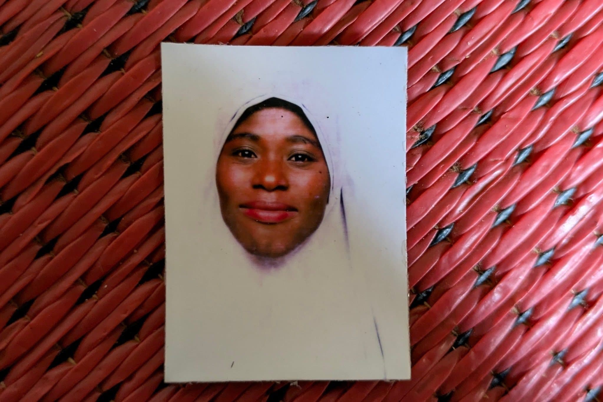 A portrait photo of a person in a light-colored headscarf on a red woven surface.