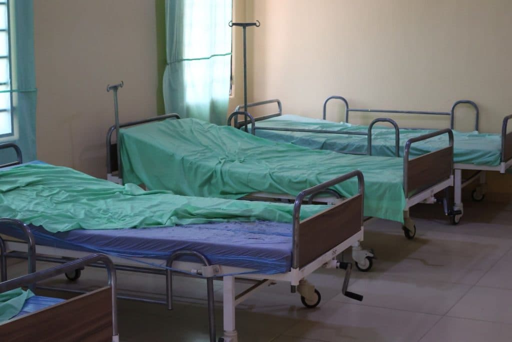 Empty hospital beds with green sheets in a sunlit room.