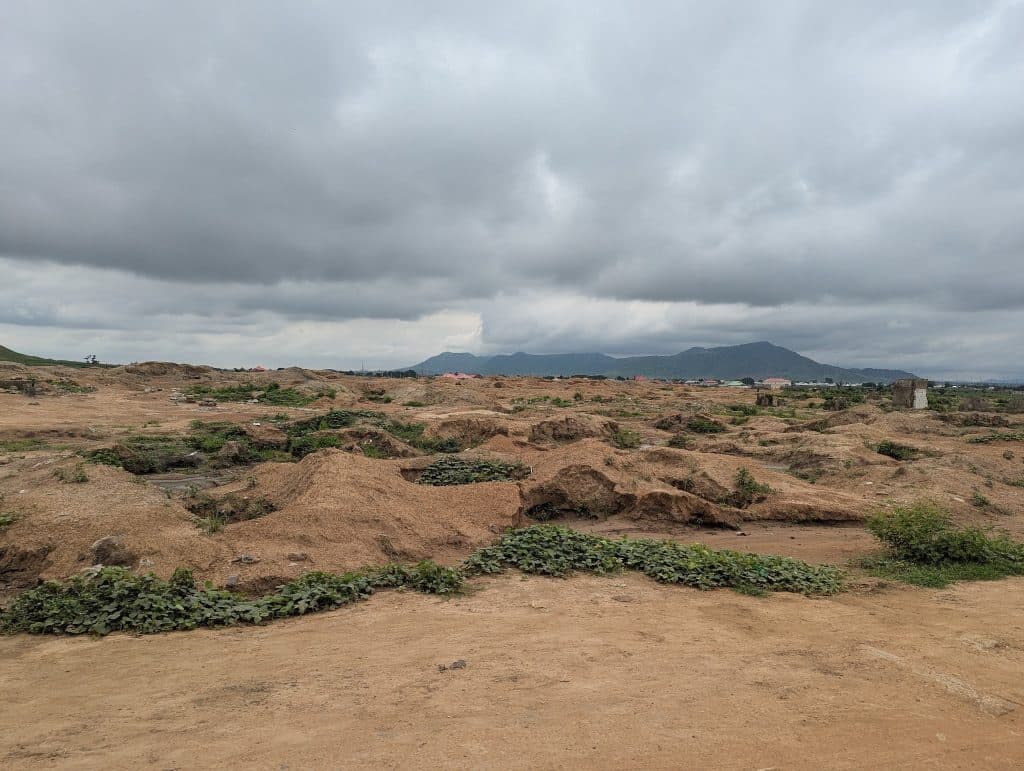 Expansive barren landscape with patches of greenery under a cloudy sky, with distant hills in the background.