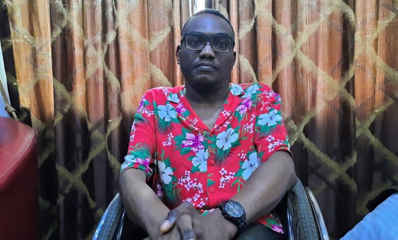 Ibrahim wears a flowery red t-shirt and sits on a wheelchair in a hotel room in Ikeja, Lagos, as he grants the interview. He is wearing glasses and a black analog watch and rests both hands on his knees.