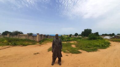 Behind Bukar Ali on his right is what used to be the Dalori II displacement camp in Maiduguri and on his left is Kofa, the host community he now calls home. Photo: ‘Kunle Adebajo/HumAngle
