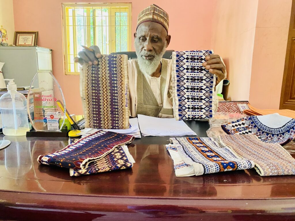 A man sitting at a desk with a table full of cloths.