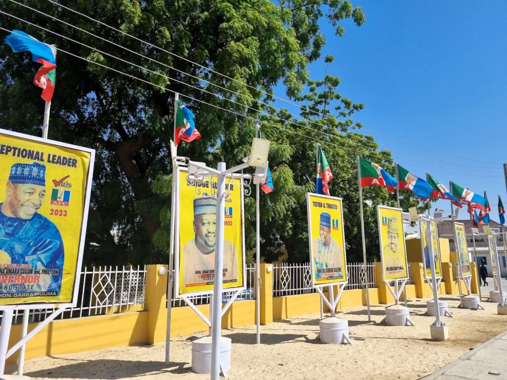 Political campaign banners lined up next to a road with party flags fluttering above.
