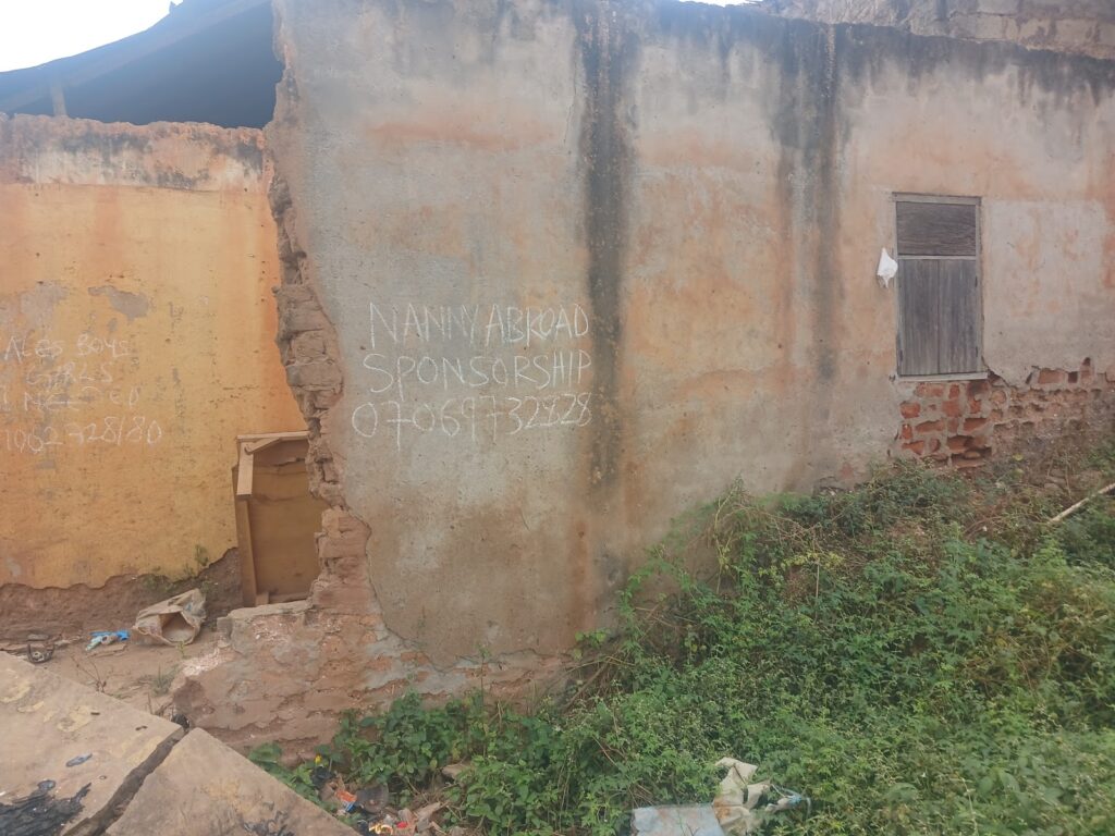 Dilapidated building with handwritten advertisements for nanny sponsorship written on the exterior wall.