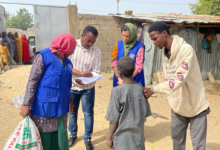 Aid workers engage with locals in a dusty village, carrying supplies and documents.