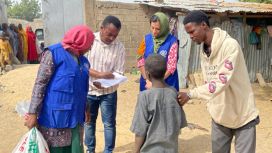 Aid workers engage with locals in a dusty village, carrying supplies and documents.