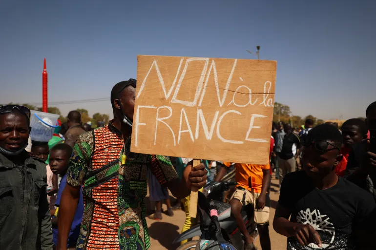 Person holding a sign with "NON à la FRANCE" written on it in a crowd.