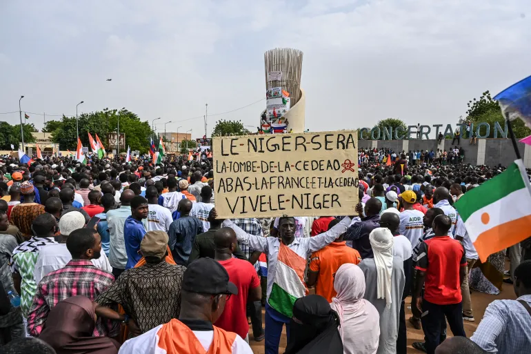 A crowd of people at a protest with a sign in French, amidst flags and banners.