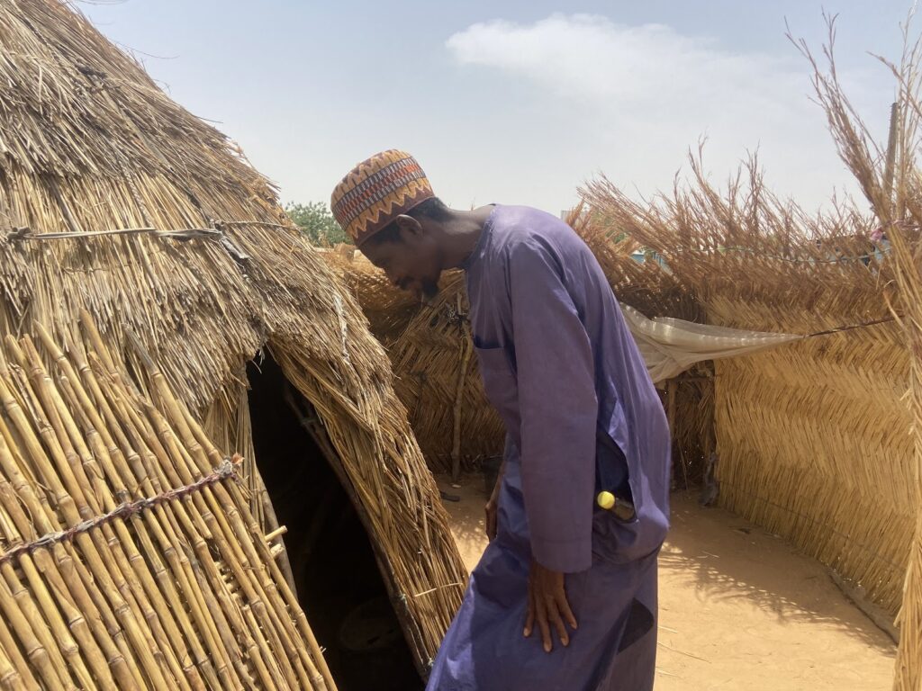 A man in traditional attire entering a thatched hut.