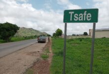 Green road sign reading "Tsafe" by a roadside with cars and lush greenery.