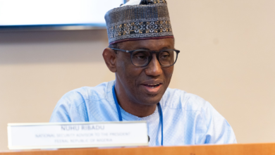 Man in traditional attire with glasses sitting behind a nameplate at a conference.