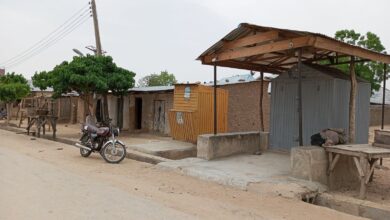 Rural street scene with a motorcycle, rustic benches, and corrugated metal shelters.