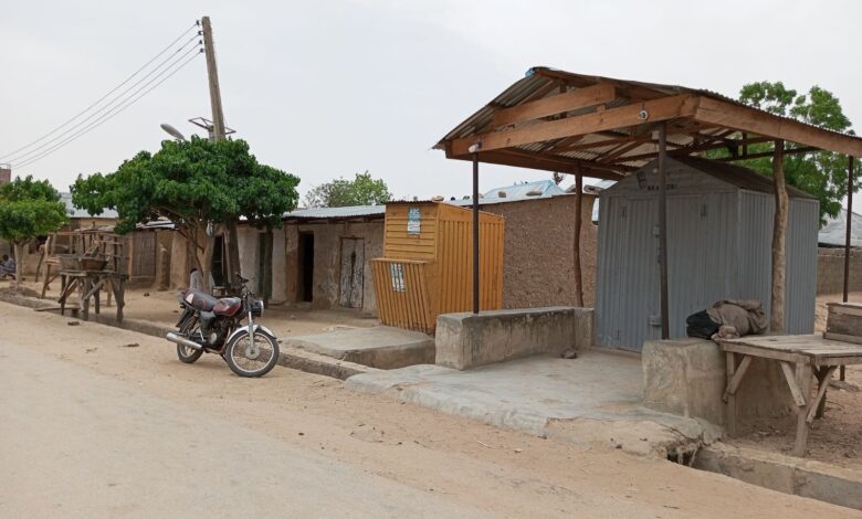 Rural street scene with a motorcycle, rustic benches, and corrugated metal shelters.