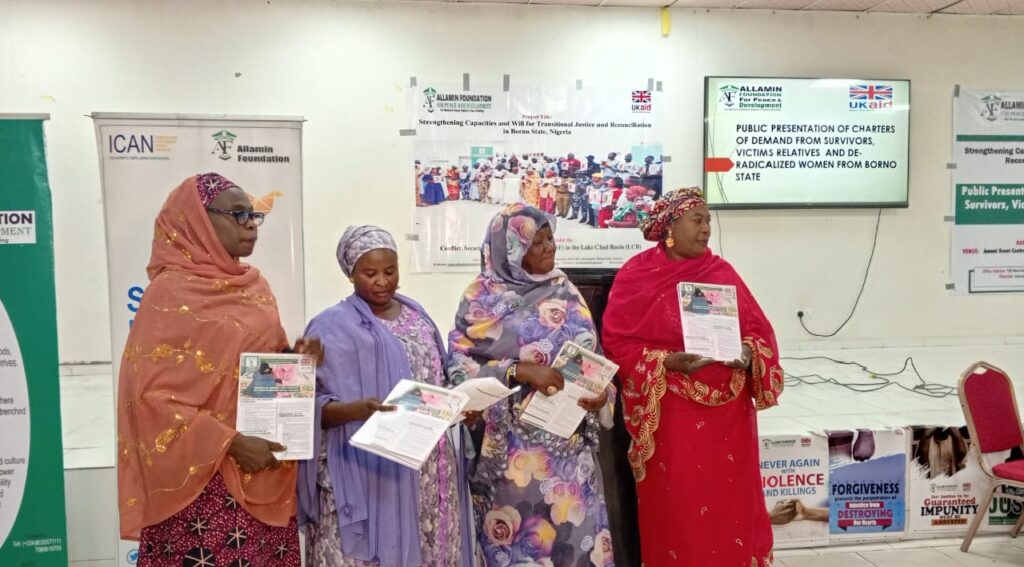 Four women in traditional attire standing with documents at an event for justice and reconciliation.